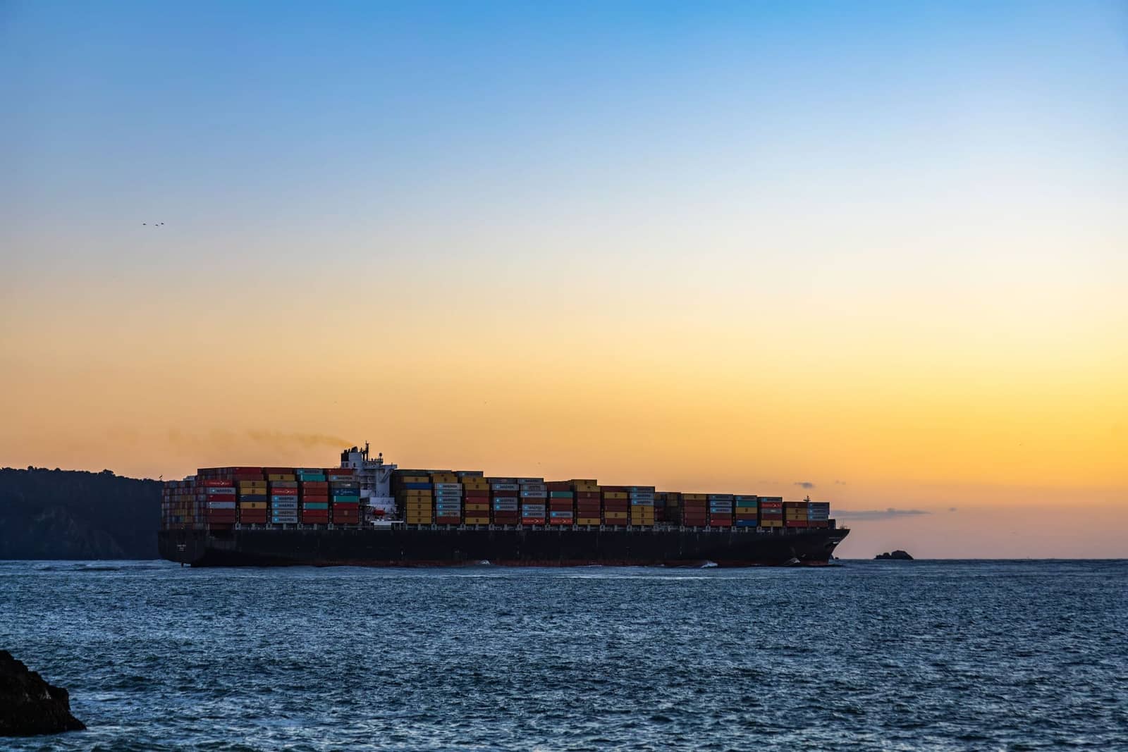 Container ship entering harbor at sunset
